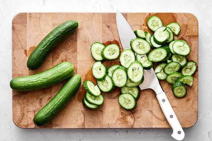 Smash and slice the cucumbers. Lay the side of your knife on the cucumber and gently smash it with your hand, just enough to break the cucumber skin down the full length of it. You could also use a meat mallet. Then slice each cucumber on an angle and add to a colander.