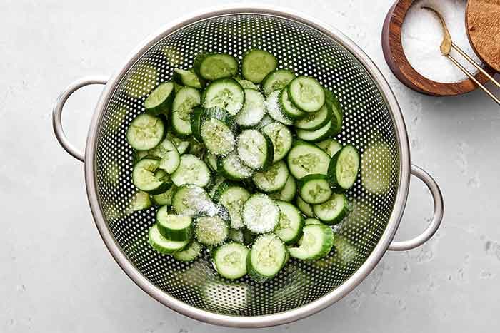 Salt and drain the cucumbers. Place the colander in your sink. Sprinkle the salt over the cucumbers, massaging it in as you toss, and let drain for 10 to 15 minutes. Rinse the cucumbers in cold water, to remove the salt, and drain again.