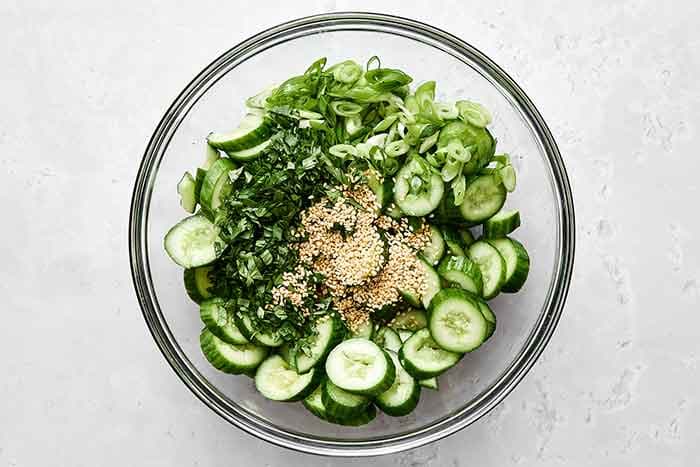 Make the salad. Place the cucumbers in a large mixing bowl. Add the green onions, cilantro, and sesame seeds.
