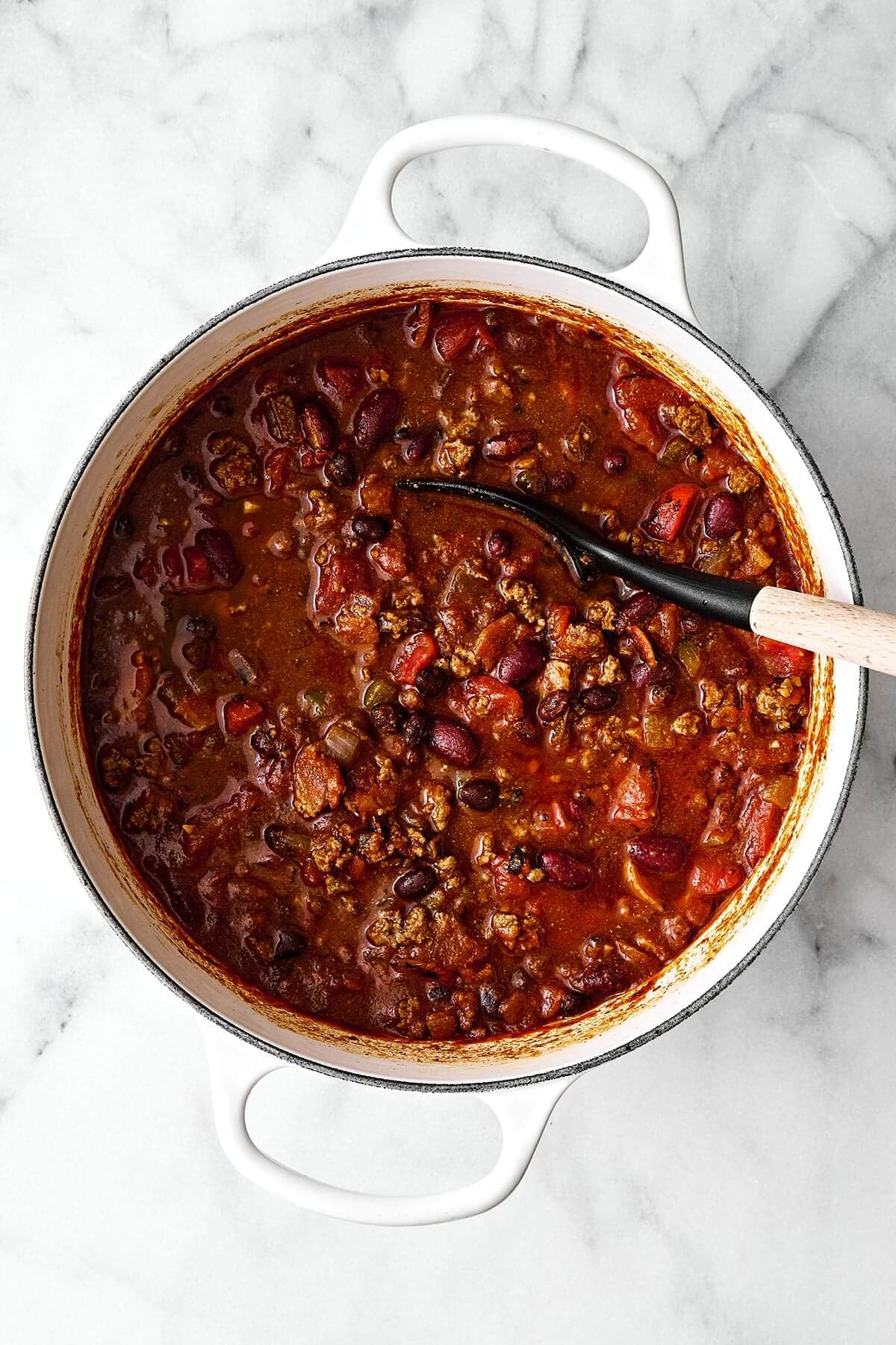 A white pot of chili with a spoon.