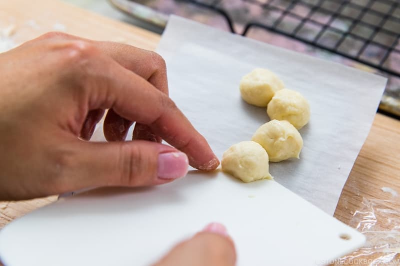 Now, form the donuts. You will need 8 balls to make each Pon de Ring donut. Use the dough scraper to transfer one ball at a time to a parchment square, forming a ring as you go. Make sure the balls are connected.