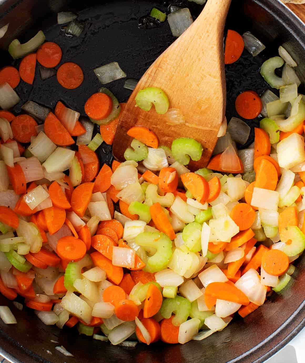 Onions, carrots, and celery in a Dutch oven with wooden spatula