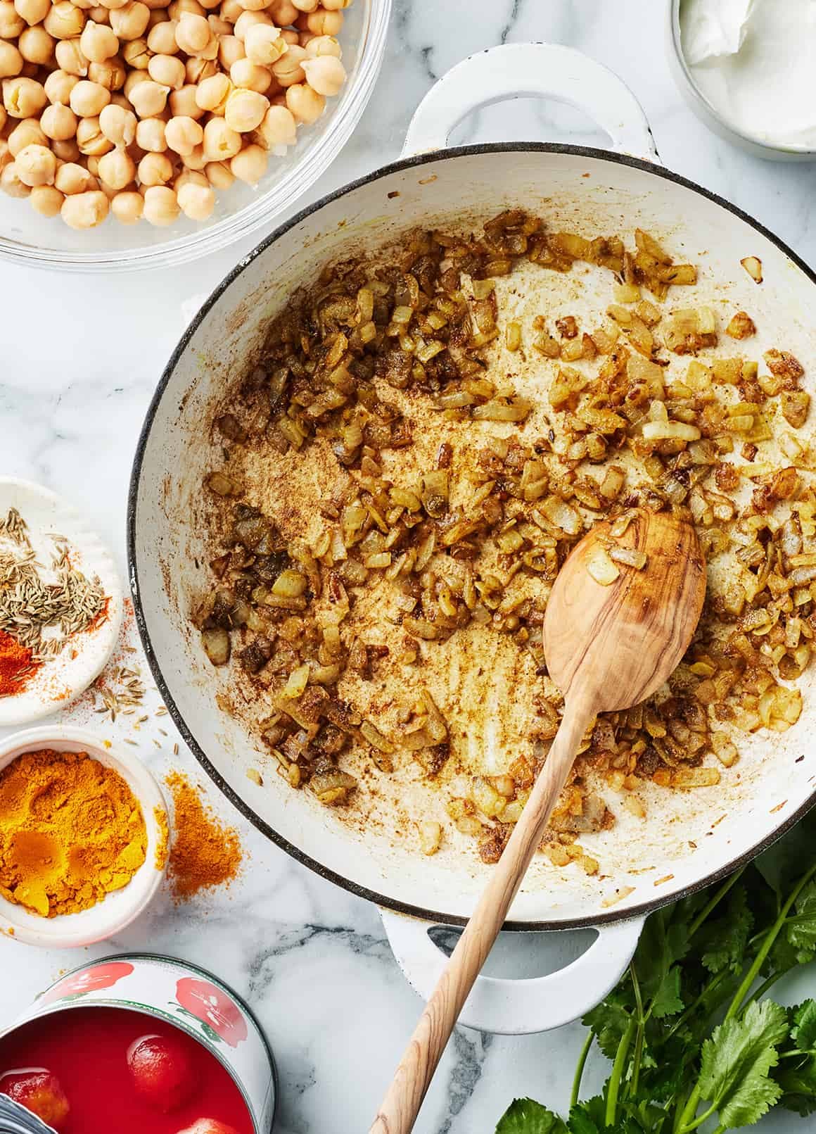 Onions and spices cooking in a skillet with wooden spoon